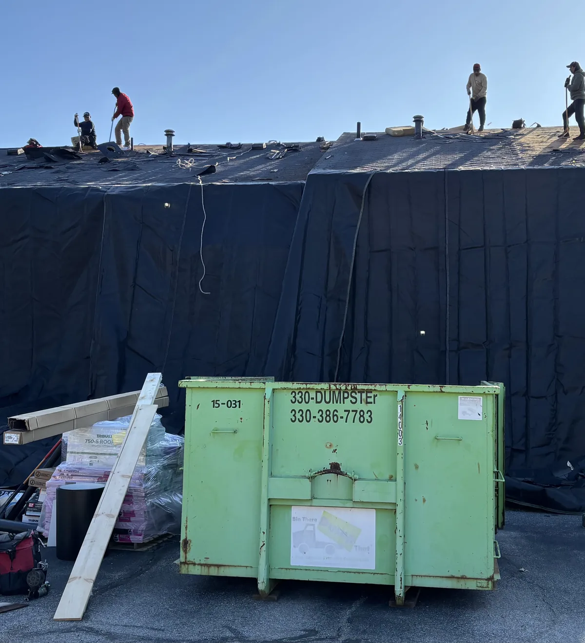 West Penn Exteriors crew tearing off a roof with the entire house draped in protective tarps and an on site dumpster for debris