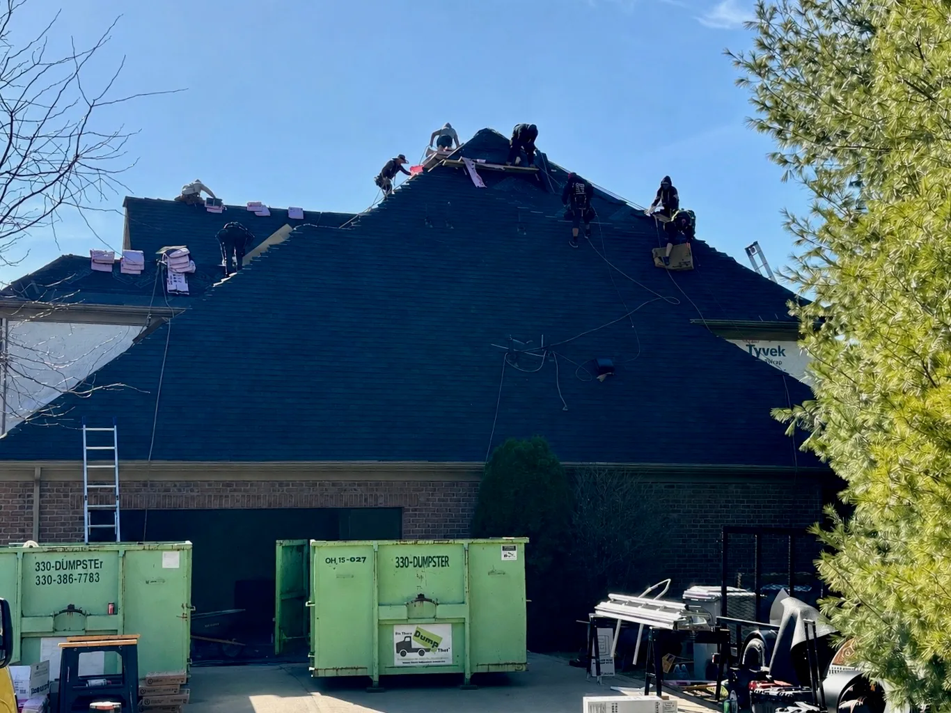 West Penn Exteriors crew installing a new roof on a large Pittsburgh home, with debris dumpsters staged on site